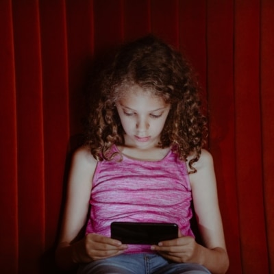 Petite fille penchée sur sa tablette mobile sur un fond rouge et sombre
