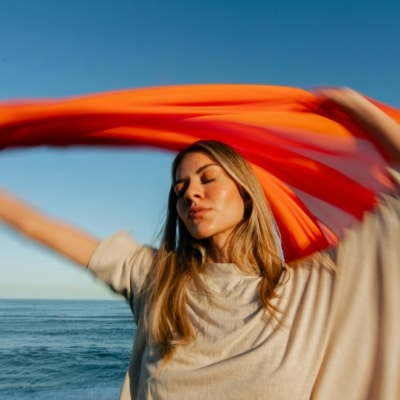 Femme agitant un tissu orange au bord de la mer