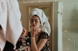 Femme qui se maquille et se prépare devant le miroir dans sa salle de bain