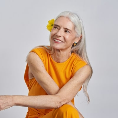 Femme aux cheveux blancs avec une robe orange et une fleur dans les cheveux posant façon shooting photo