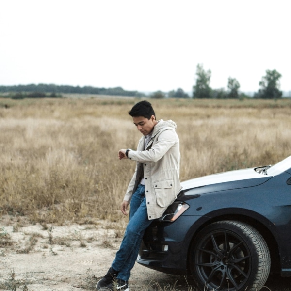 Homme adossé sur une voiture au milieu de la nature et qui regarde l'heure à travers sa montre