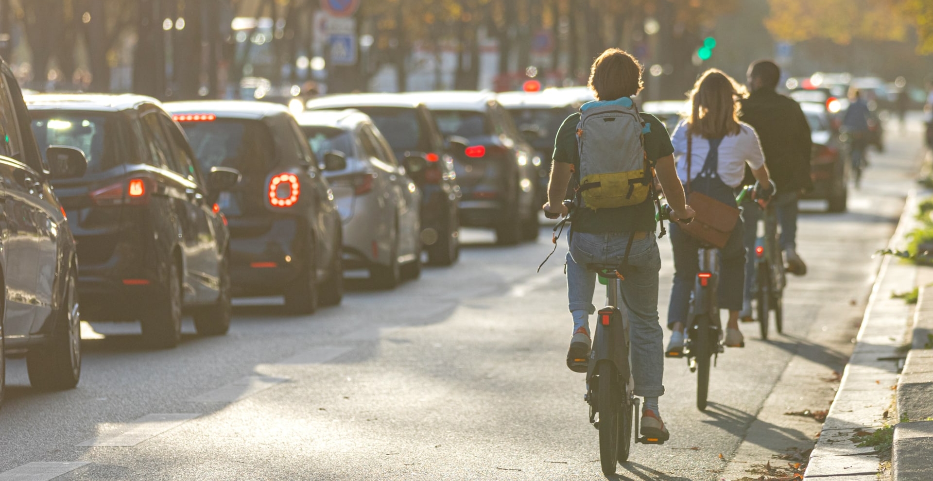 3 personnes de dos en vélo sur la route à coté de voiture en embouteillage