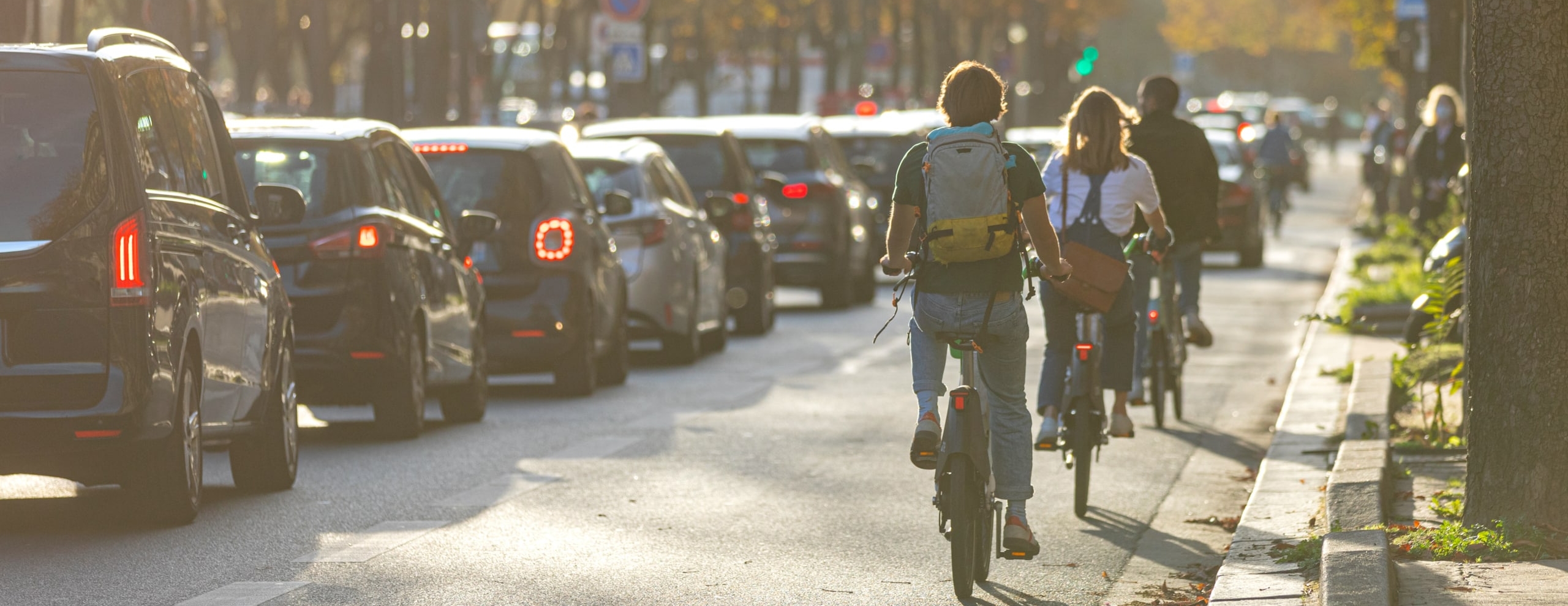 3 personnes de dos en vélo sur la route à coté de voiture en embouteillage